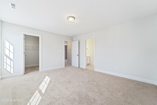 unfurnished bedroom with a spacious closet, a closet, ensuite bathroom, and light carpet