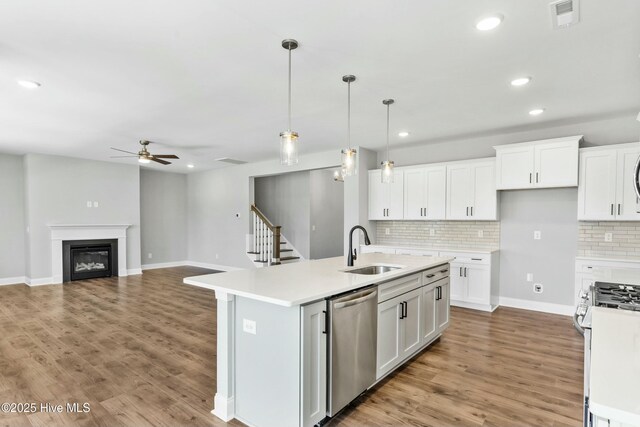 kitchen featuring a center island with sink, backsplash, dishwasher, decorative light fixtures, and white cabinets