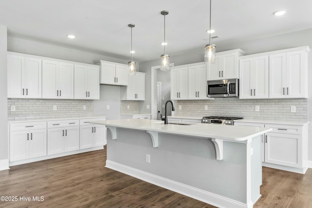 kitchen with an island with sink, sink, white cabinets, dark hardwood / wood-style flooring, and hanging light fixtures