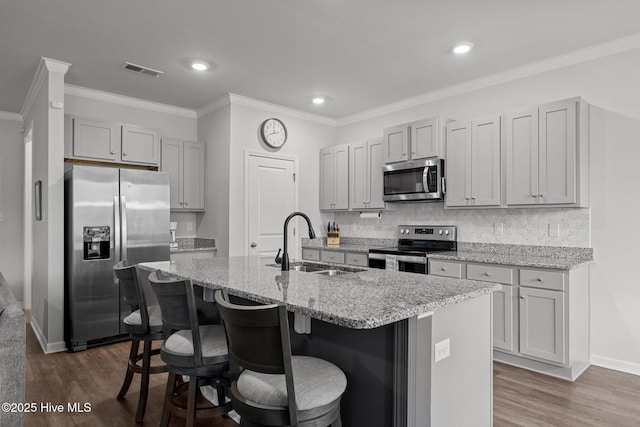 kitchen with sink, dark hardwood / wood-style floors, an island with sink, appliances with stainless steel finishes, and light stone counters