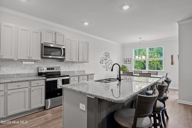 kitchen with stainless steel appliances, light stone counters, a kitchen island with sink, and sink