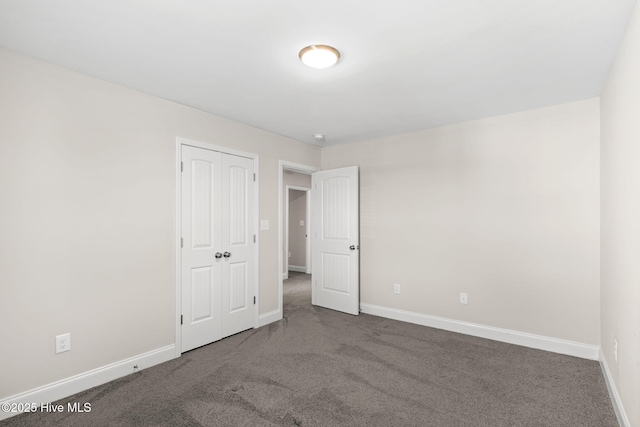 unfurnished bedroom with dark colored carpet and a closet