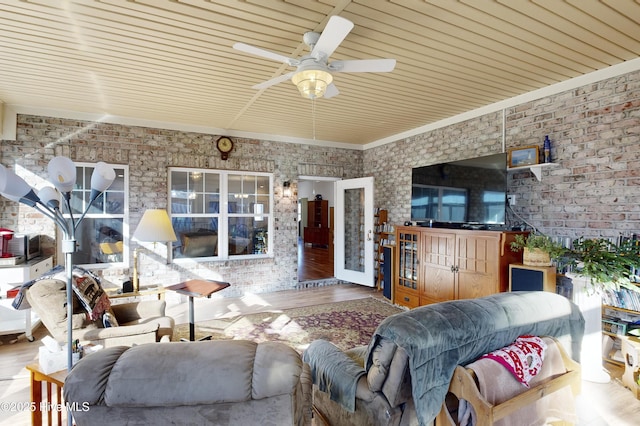 living room featuring ceiling fan, hardwood / wood-style floors, and brick wall