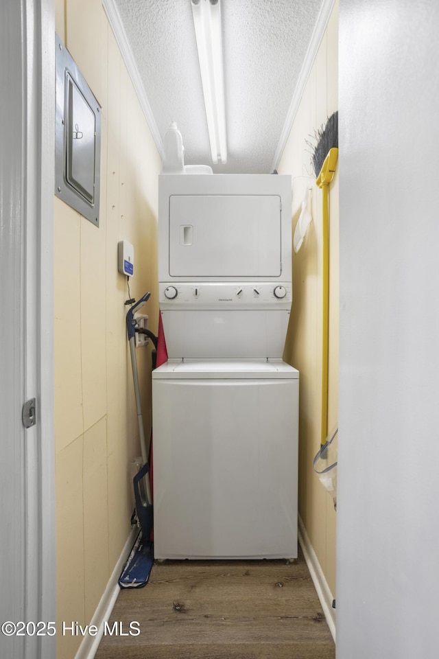 clothes washing area with wood walls, ornamental molding, a textured ceiling, wood-type flooring, and stacked washer / dryer