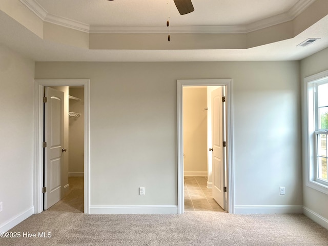 unfurnished bedroom featuring a tray ceiling, a walk in closet, light carpet, a closet, and ornamental molding