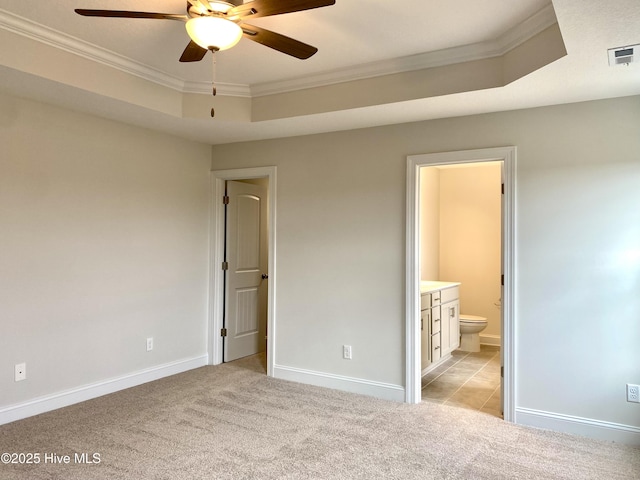 unfurnished bedroom with ensuite bathroom, ceiling fan, a raised ceiling, and ornamental molding