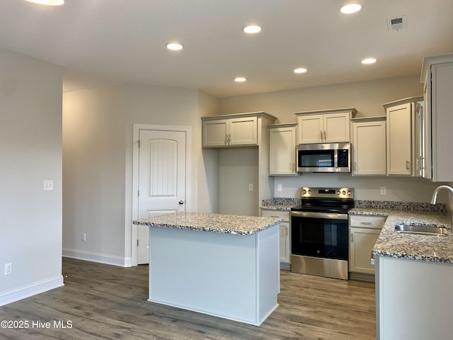 kitchen featuring appliances with stainless steel finishes, light stone counters, sink, dark hardwood / wood-style floors, and a kitchen island