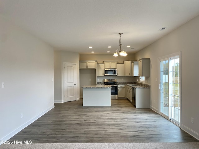 kitchen with a center island, light stone counters, wood-type flooring, pendant lighting, and appliances with stainless steel finishes