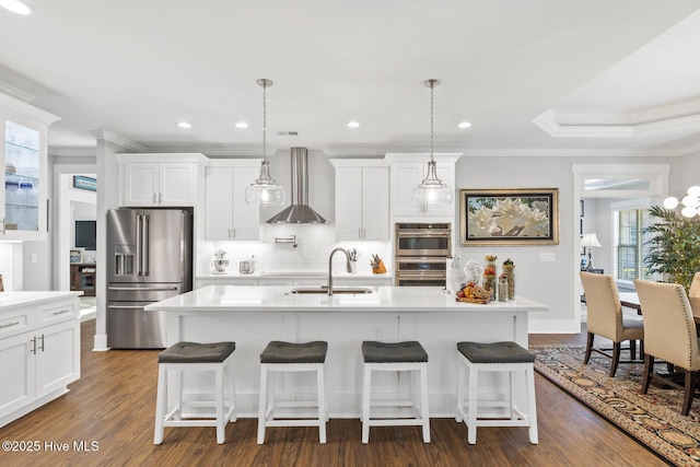 kitchen featuring an island with sink, stainless steel appliances, dark hardwood / wood-style floors, wall chimney range hood, and pendant lighting