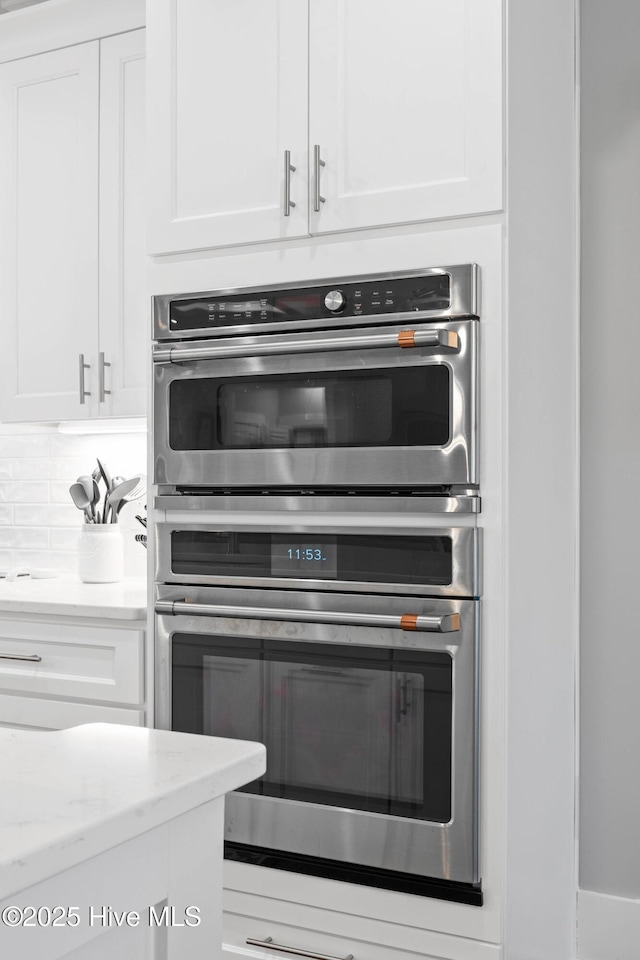 kitchen featuring light stone counters, white cabinetry, decorative backsplash, and stainless steel double oven