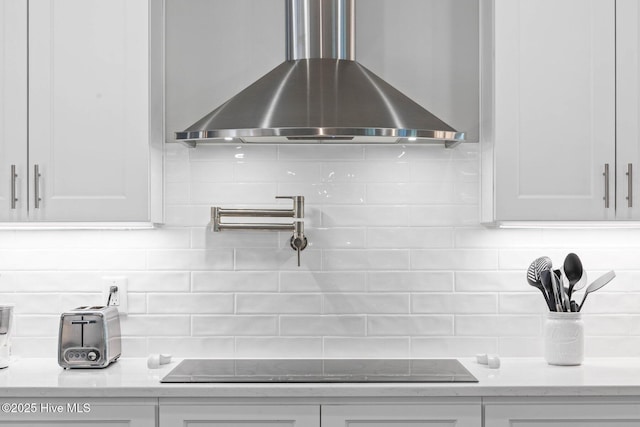 details featuring white cabinetry, backsplash, wall chimney range hood, and black electric cooktop