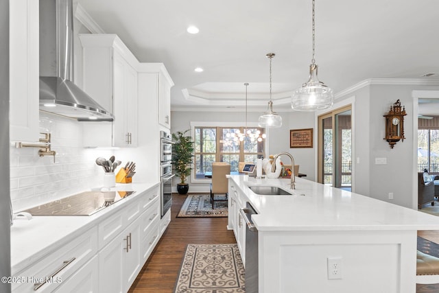 kitchen with sink, wall chimney range hood, black electric stovetop, and a center island with sink