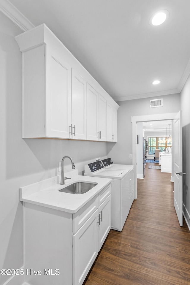 clothes washing area with washer and dryer, cabinets, dark wood-type flooring, sink, and crown molding