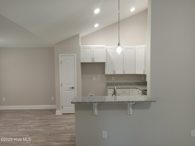 kitchen featuring a kitchen bar, kitchen peninsula, light stone counters, pendant lighting, and white cabinetry