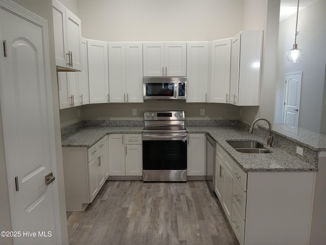 kitchen featuring white cabinets, hanging light fixtures, sink, appliances with stainless steel finishes, and kitchen peninsula