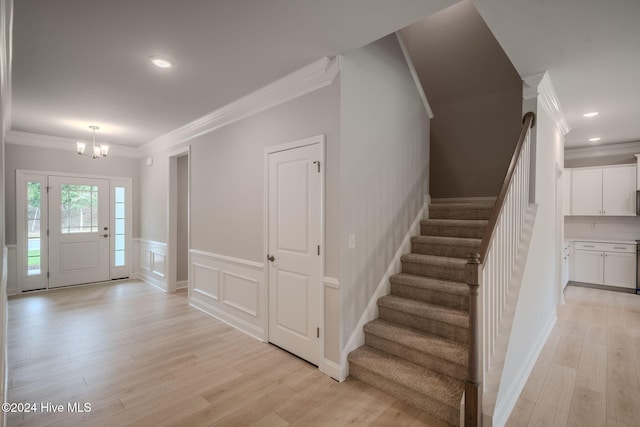 foyer with a wainscoted wall, crown molding, stairs, light wood finished floors, and an inviting chandelier