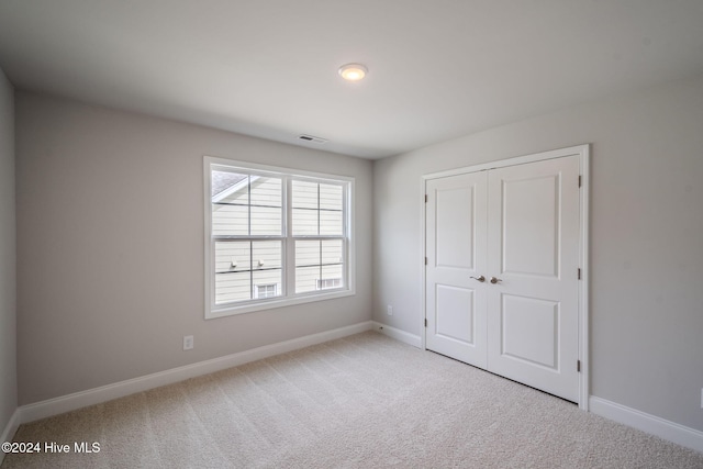 unfurnished bedroom featuring baseboards, a closet, visible vents, and light colored carpet