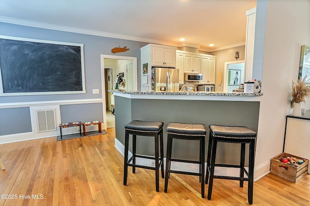 kitchen featuring white cabinetry, light stone counters, a breakfast bar area, and appliances with stainless steel finishes