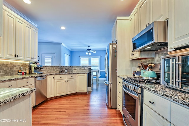 kitchen featuring appliances with stainless steel finishes, kitchen peninsula, ornamental molding, ceiling fan, and light stone counters