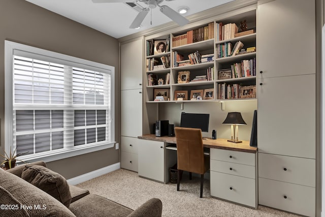 home office with baseboards, a ceiling fan, built in desk, and light carpet