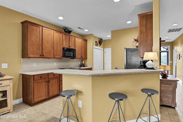 kitchen featuring light tile patterned floors, visible vents, a breakfast bar, freestanding refrigerator, and black microwave