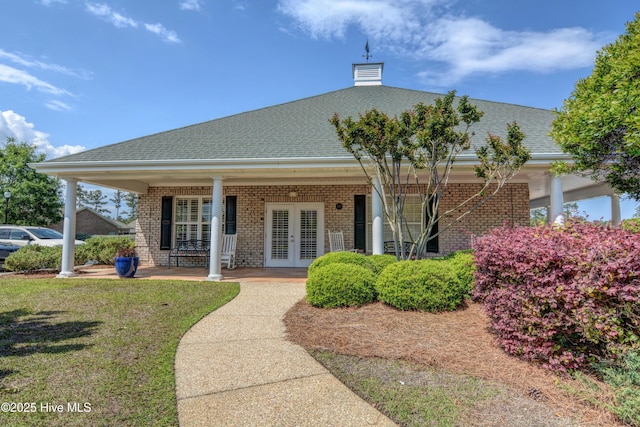 view of front facade with brick siding, a porch, a front yard, french doors, and a chimney