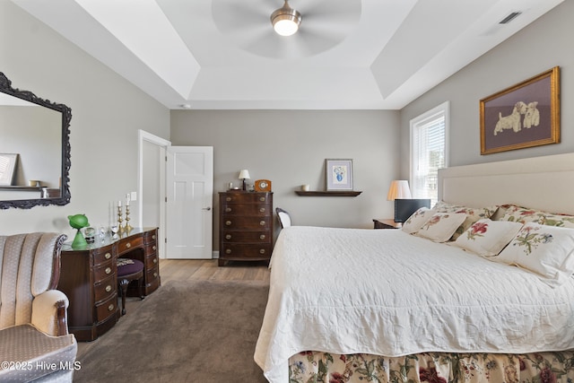 bedroom featuring a tray ceiling, ceiling fan, and dark colored carpet