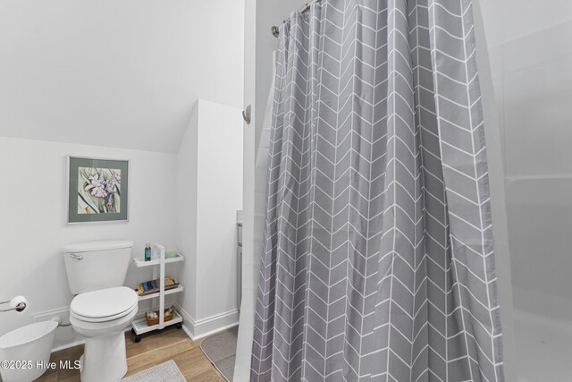 bathroom with toilet, a shower with curtain, vaulted ceiling, and hardwood / wood-style floors