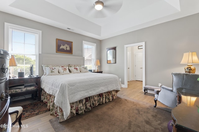 bedroom featuring light hardwood / wood-style flooring, a raised ceiling, and ceiling fan