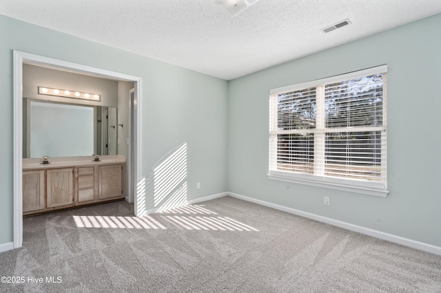 unfurnished bedroom with sink, light colored carpet, a textured ceiling, and ensuite bath