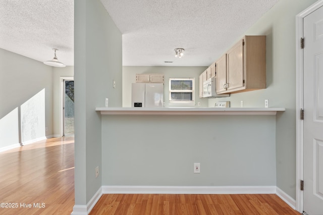 kitchen featuring light brown cabinets, light wood-type flooring, white appliances, and a textured ceiling