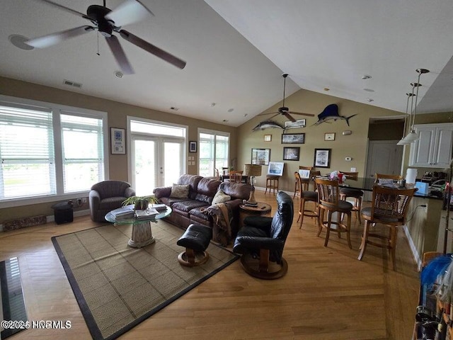 living room with french doors, lofted ceiling, a healthy amount of sunlight, and light wood-type flooring