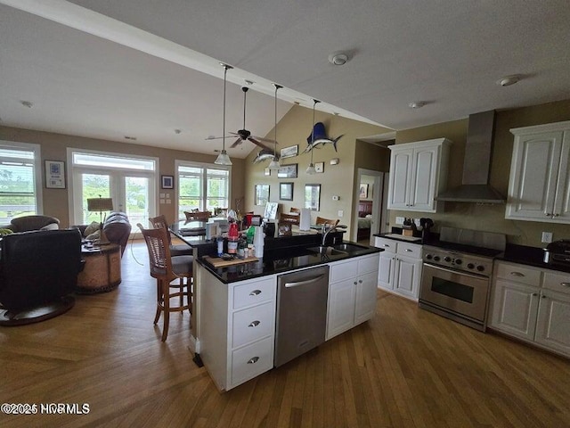 kitchen featuring white cabinetry, sink, a breakfast bar area, stainless steel appliances, and wall chimney range hood