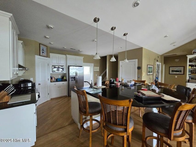 kitchen with dark wood-type flooring, vaulted ceiling, appliances with stainless steel finishes, pendant lighting, and white cabinets