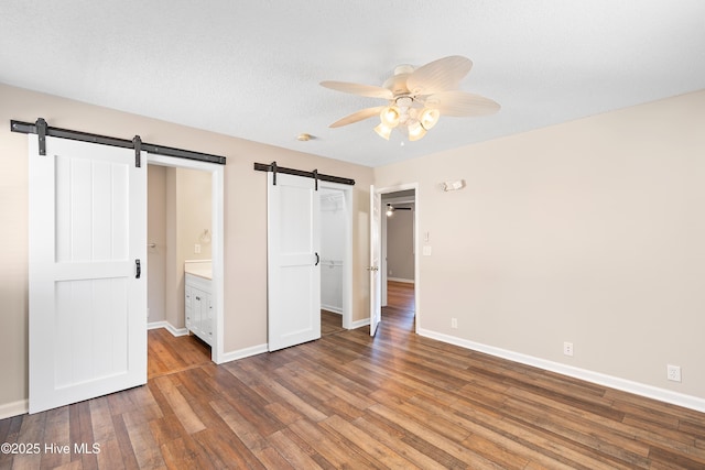 unfurnished bedroom with a textured ceiling, wood-type flooring, ceiling fan, ensuite bathroom, and a barn door