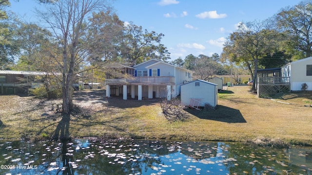 back of property with a yard, a storage unit, and a deck with water view