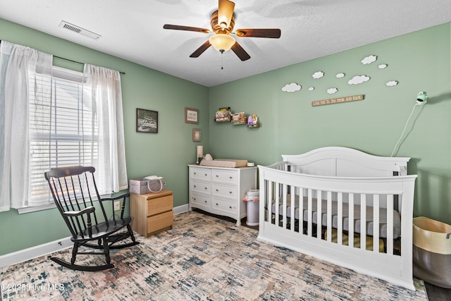 bedroom with a textured ceiling, ceiling fan, and a crib