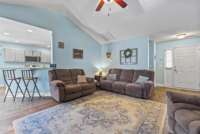 living room with a textured ceiling, ceiling fan, lofted ceiling, and dark wood-type flooring