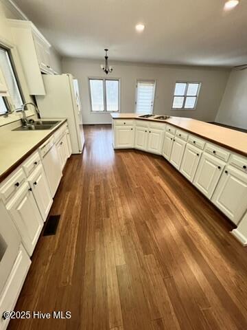 kitchen featuring kitchen peninsula, sink, white cabinetry, dark wood-type flooring, and a chandelier