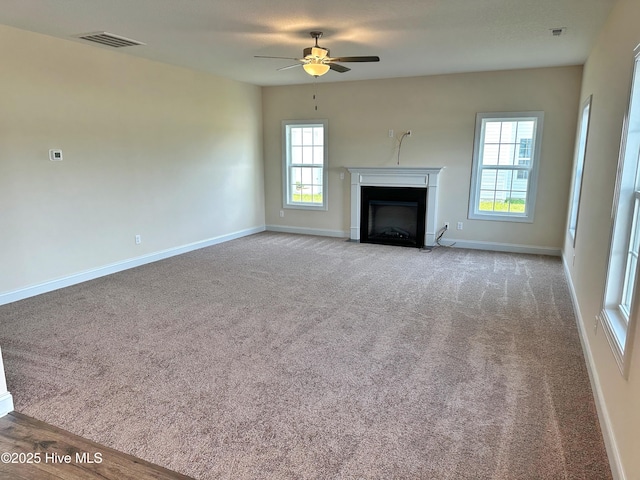 unfurnished living room featuring ceiling fan, light carpet, and a wealth of natural light