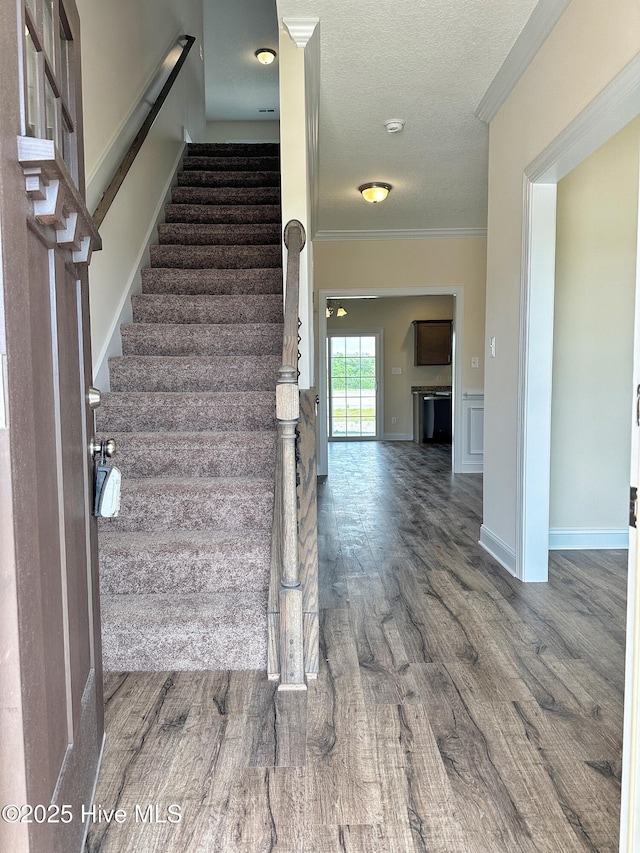 stairway featuring crown molding, wood-type flooring, and a textured ceiling