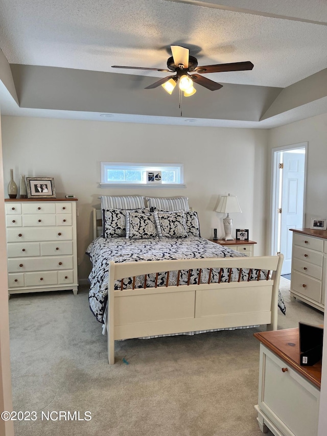 carpeted bedroom featuring a textured ceiling, a raised ceiling, and ceiling fan