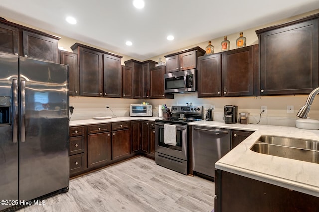 kitchen with a sink, appliances with stainless steel finishes, light wood-style floors, dark brown cabinetry, and recessed lighting