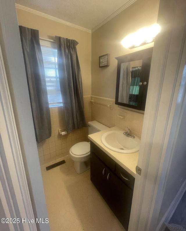 bathroom with tile patterned flooring, crown molding, toilet, vanity, and tile walls