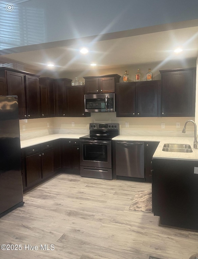 kitchen with appliances with stainless steel finishes, dark brown cabinetry, light hardwood / wood-style floors, and sink