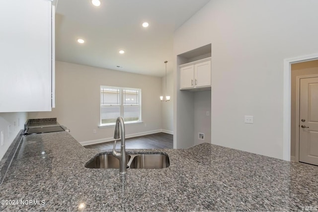 kitchen featuring recessed lighting, hanging light fixtures, white cabinetry, a sink, and dark stone countertops