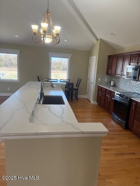 kitchen featuring pendant lighting, an inviting chandelier, a center island with sink, sink, and electric range