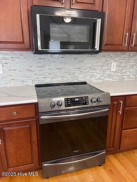 kitchen featuring tasteful backsplash, light stone counters, stainless steel stove, and light wood-type flooring