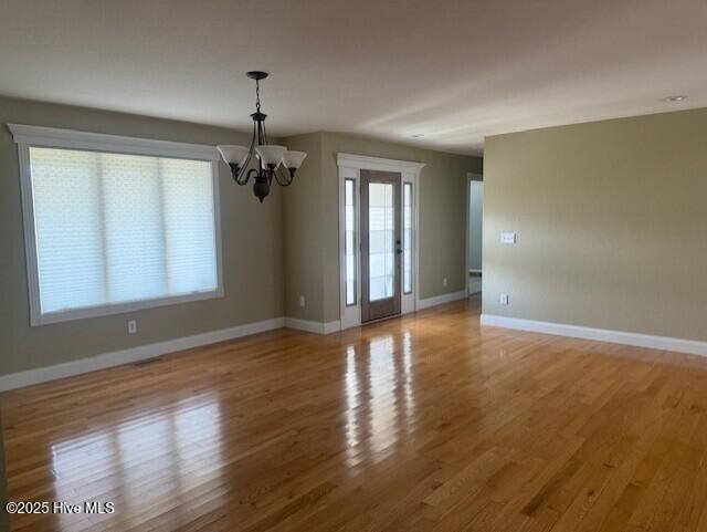 empty room with light hardwood / wood-style flooring, a healthy amount of sunlight, and an inviting chandelier