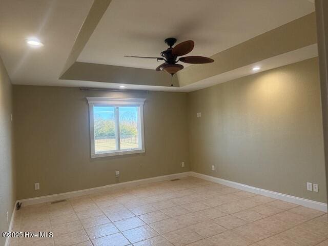 empty room featuring ceiling fan, light tile patterned flooring, and a tray ceiling